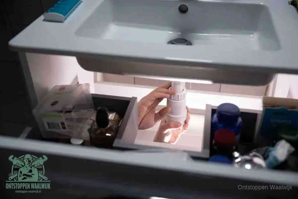Een pompfles met zeep boven een wastafel, de heet water en afwasmiddel-methode om een vetprop in de afvoer los te maken in Waalwijk