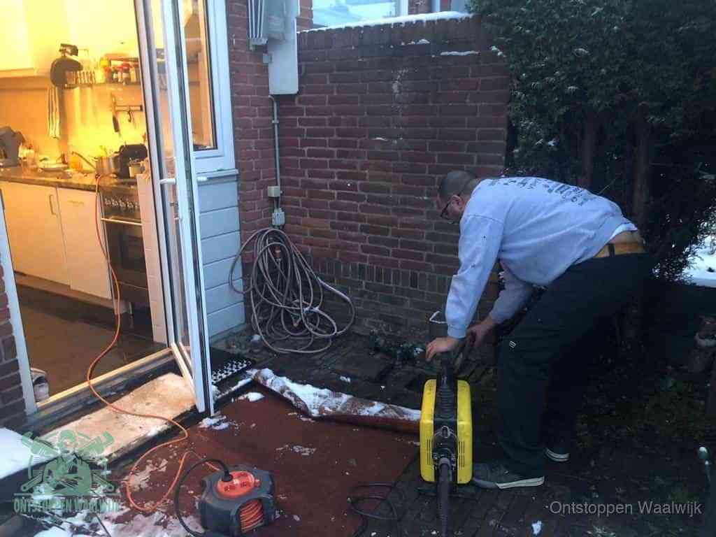 Een monteur werkt buiten bij een open riool-/grondput met een elektrische ontstoppingsmachine om een verborgen afvoerprobleem op te sporen in Waalwijk