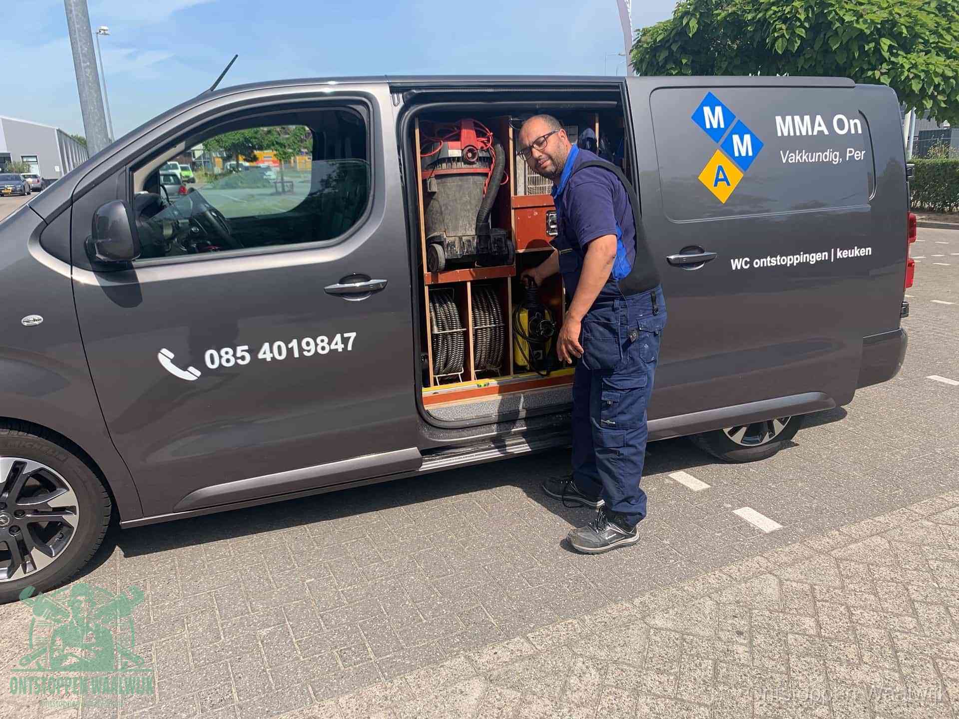 Een monteur bij de open schuifdeur van zijn bedrijfsbus op een parkeerplaats, klaar om de oorzaak van terugkerende afvoerverstoppingen aan te pakken in Waalwijk