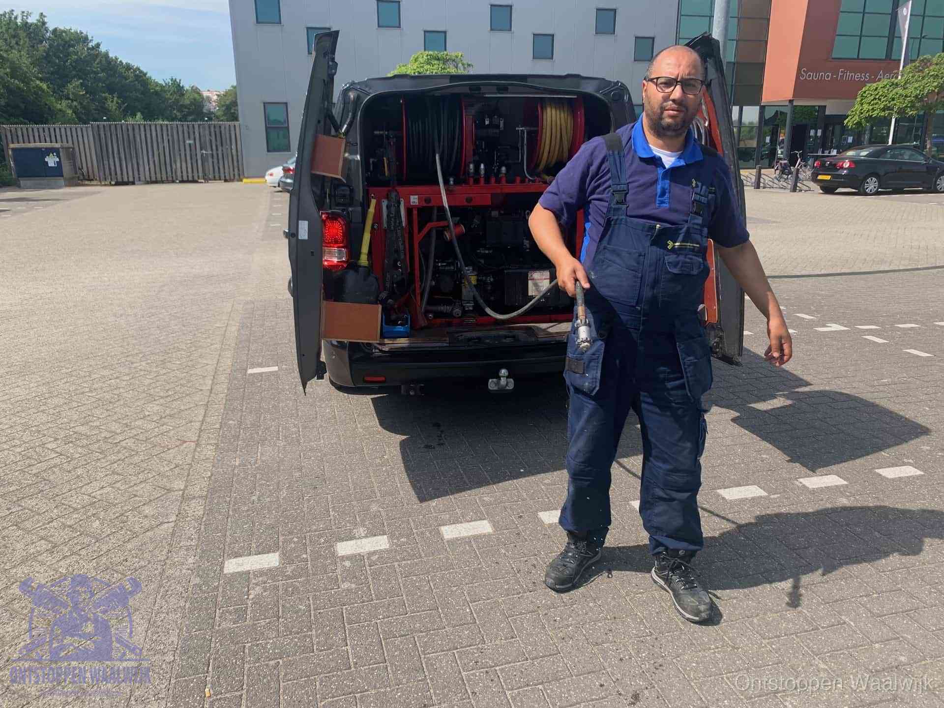 Een monteur bij zijn bestelbus met een hogedruk- en rioolreinigingsunit, klaar om de oorzaak van terugkerende wc-verstoppingen aan te pakken in Waalwijk