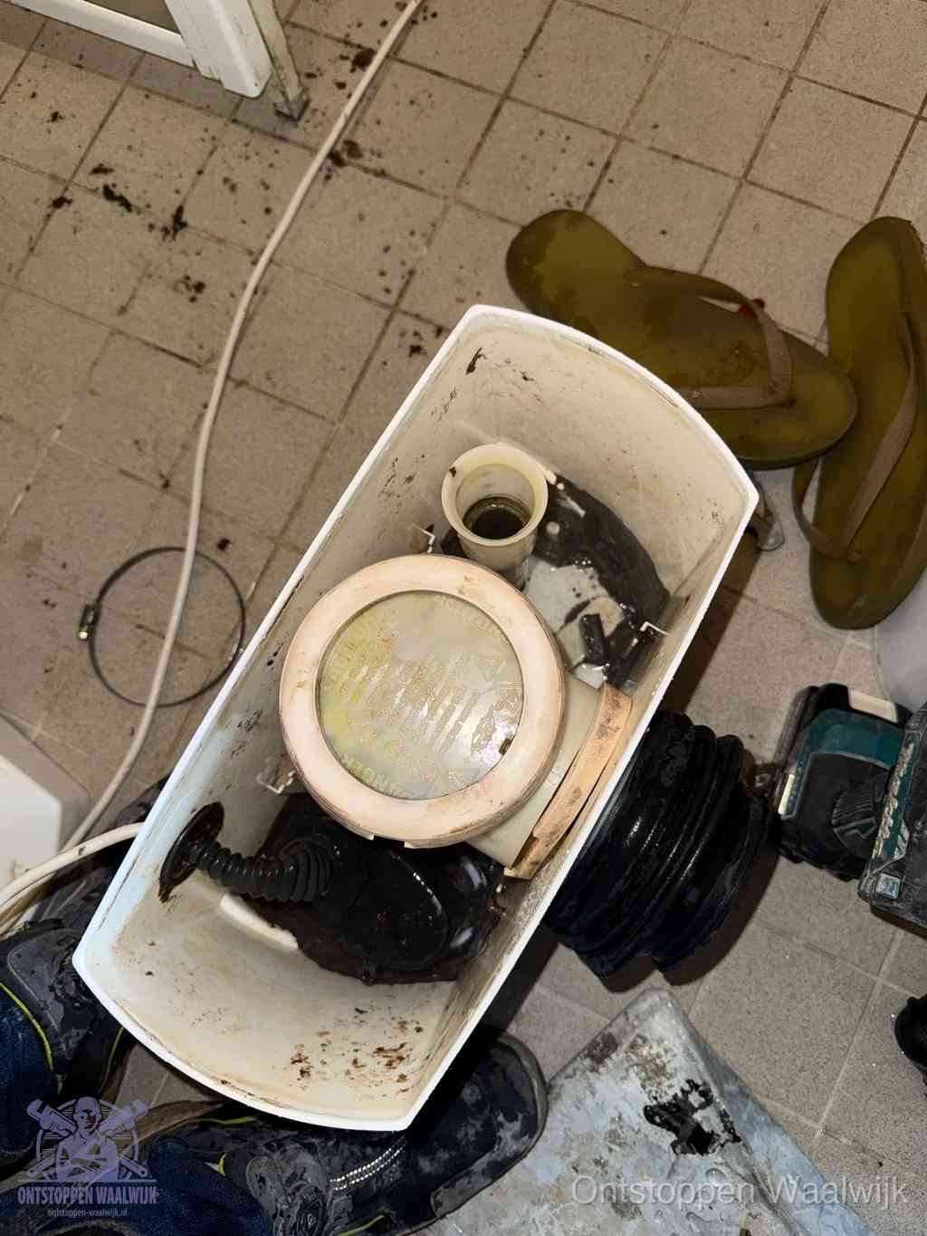 Een gedemonteerde toiletpot op de vloer met ontstoppingsveer en gereedschap ernaast, het verwijderen van een vastzittend voorwerp uit de wc in Waalwijk